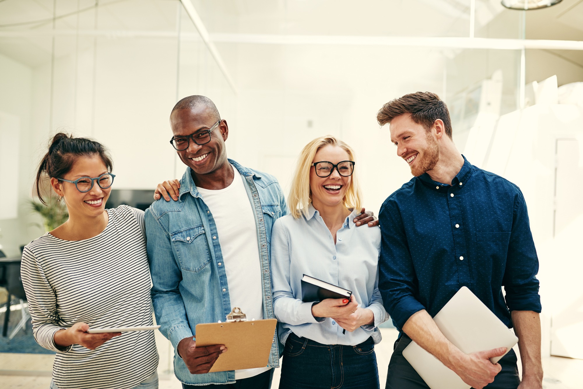 Group of diverse young businesspeople smiling and laughing while standing side by side together in a modern office
